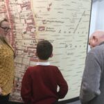 A gentleman and school boy looking at the wall map together with member of the Archive staff