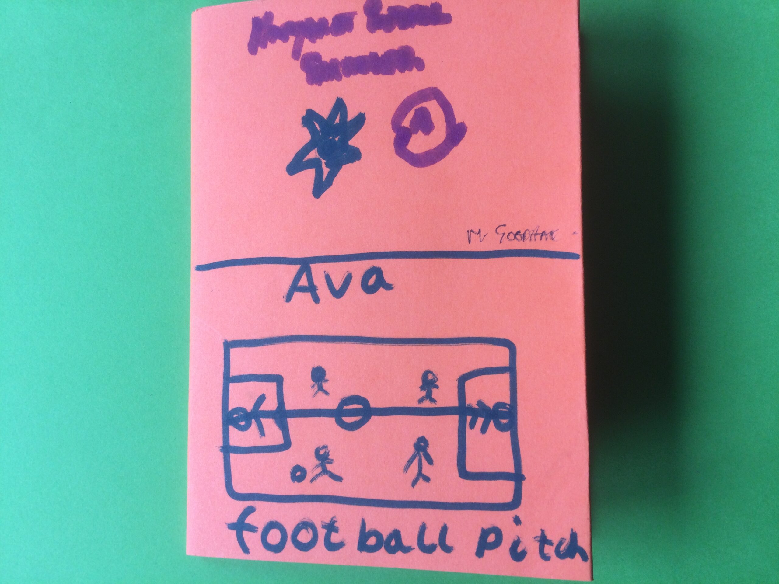 A pink paper booklet with hand drawn image of a football pitch