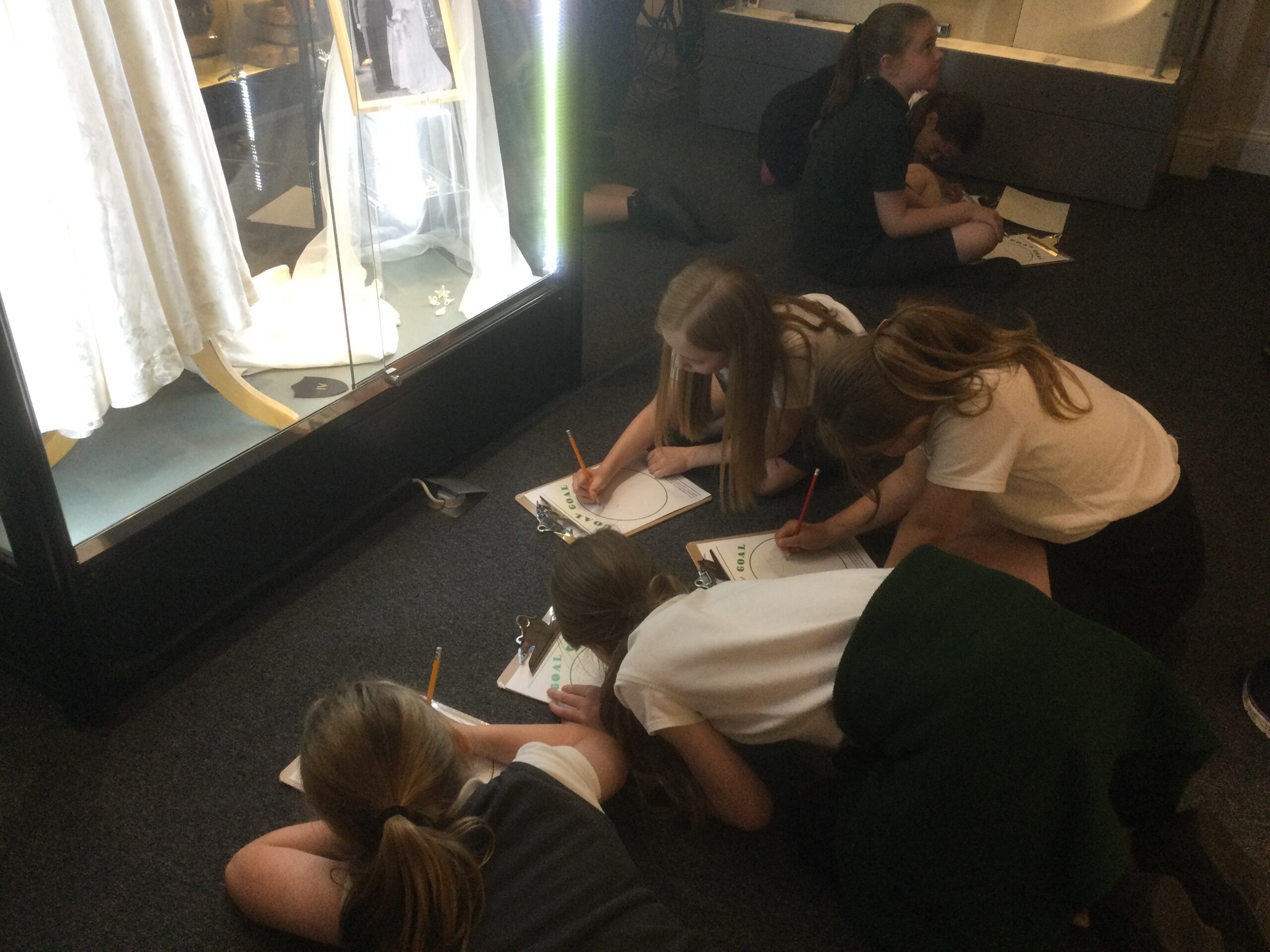 School children crouched down on the floor drawing an exhibit in a well-lit display case