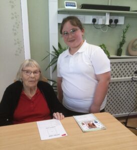 A school child in a white T-shirt stands next to a seated woman in a maroon top and black cardigan