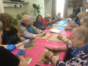 A group of adults, each with a board and rolling pin, rolling out pieces of clay