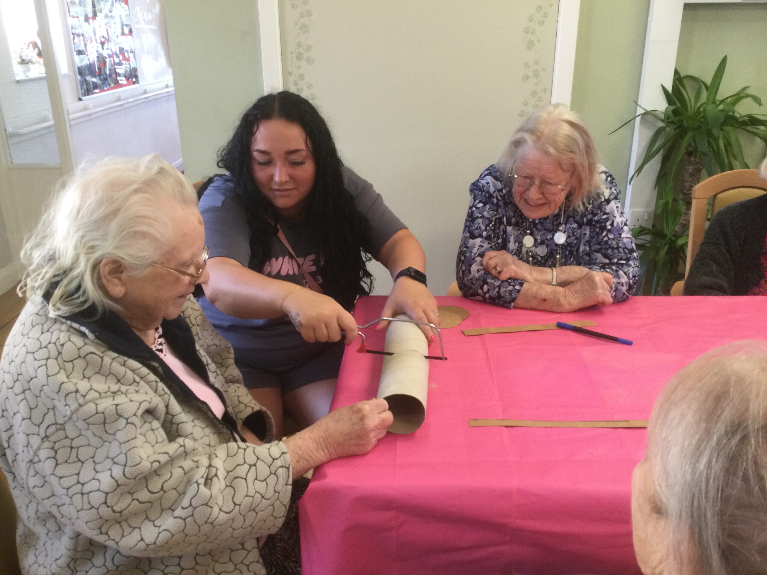 Two women look on as a third cuts through a stiff cardboard tube with a hacksaw