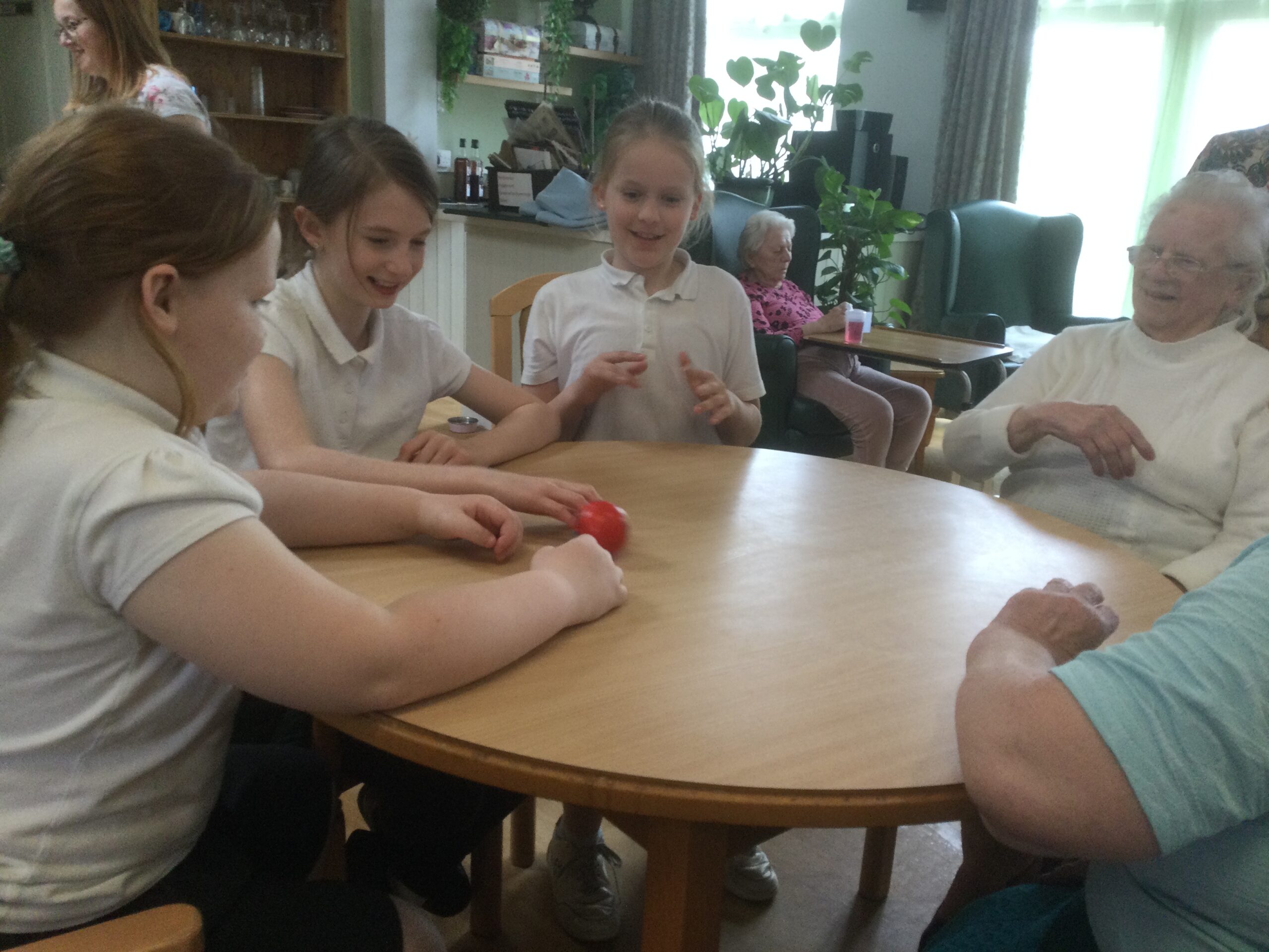 Three school girls and two residents rolling a ball across a table to one another