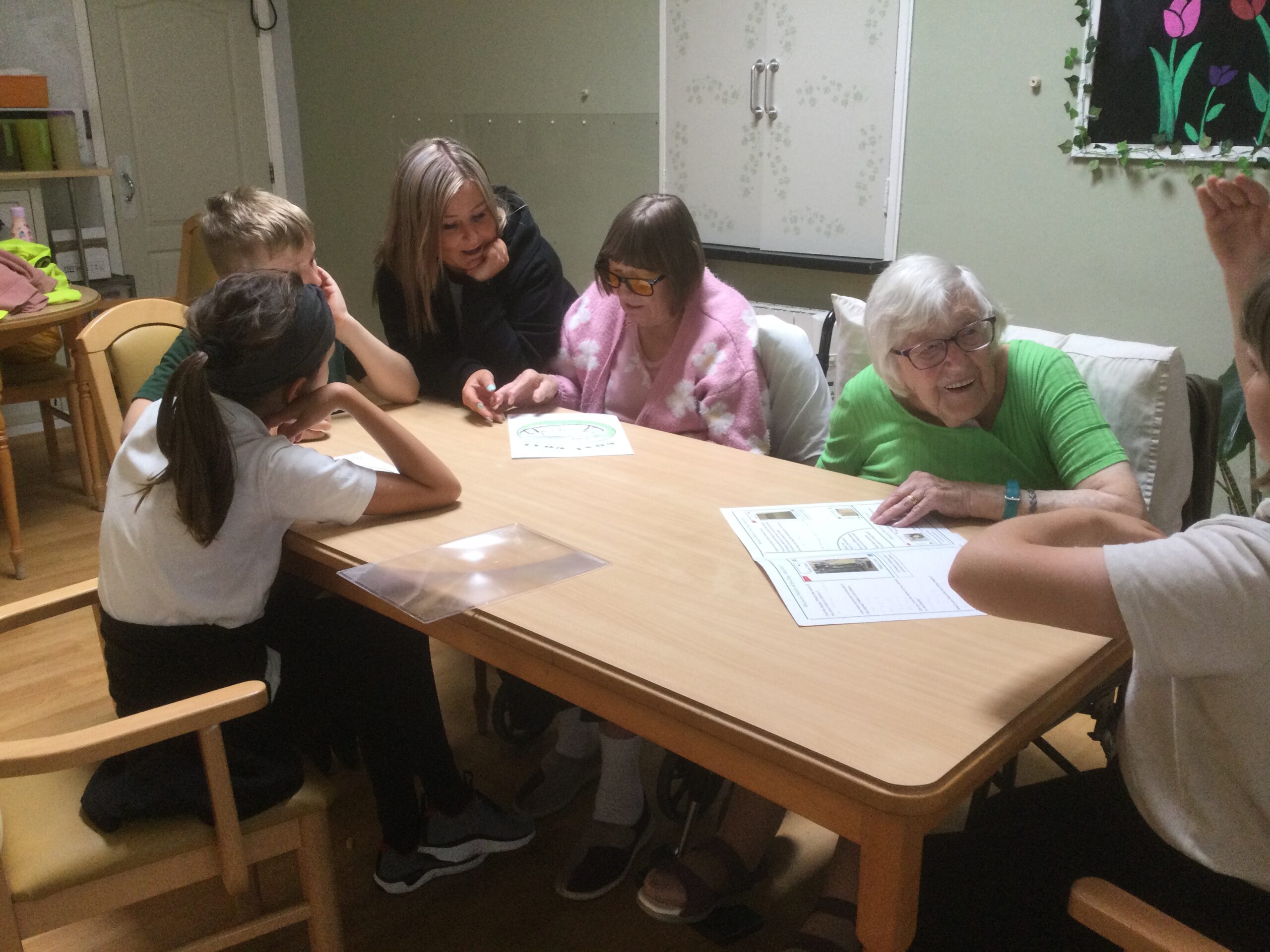 School children seated at a table along with three adults, all looking at some worksheets on the table in front of them