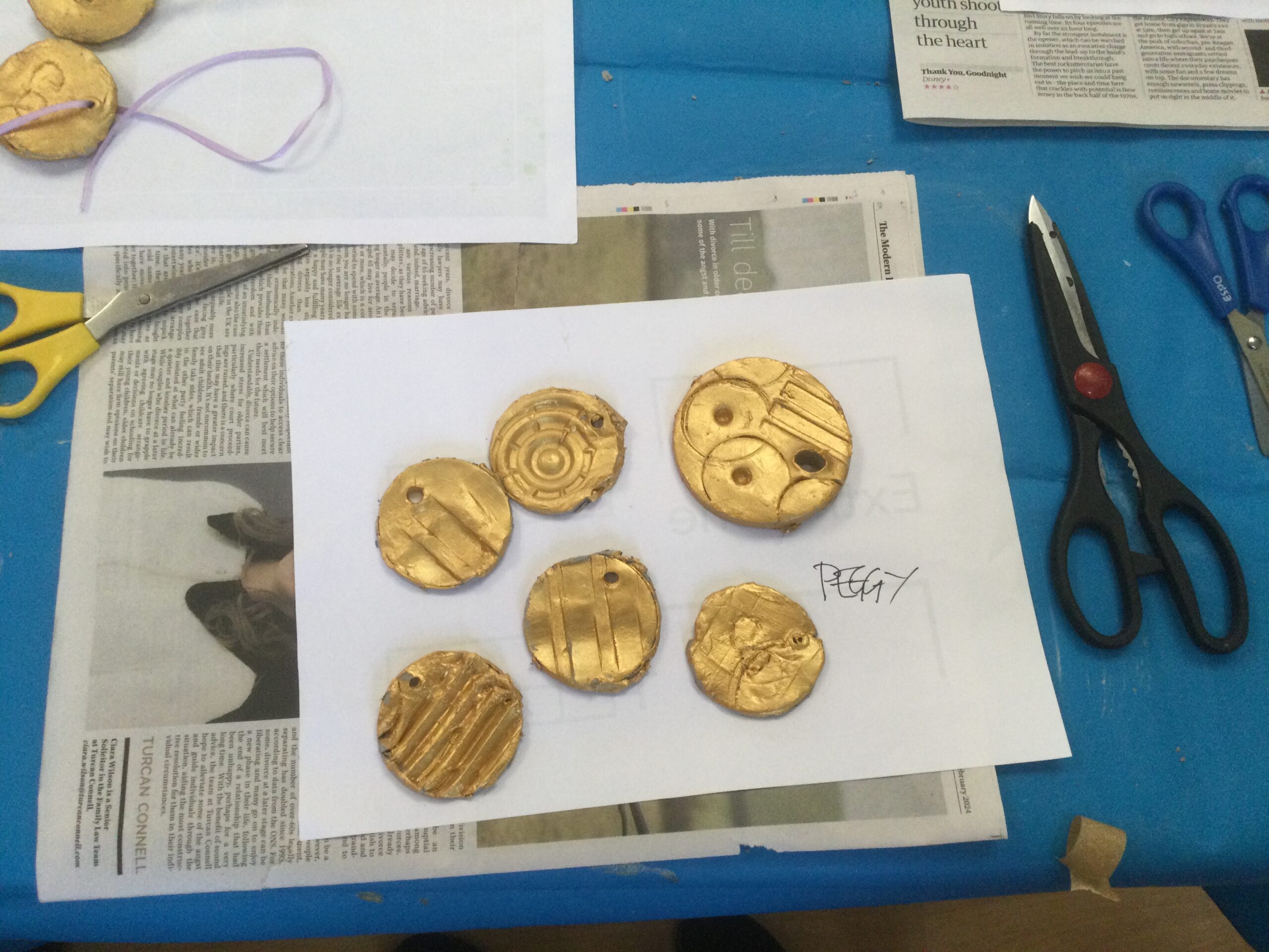 Six gold medals on a white sheet of paper, with more medals top left and pairs of scissors around