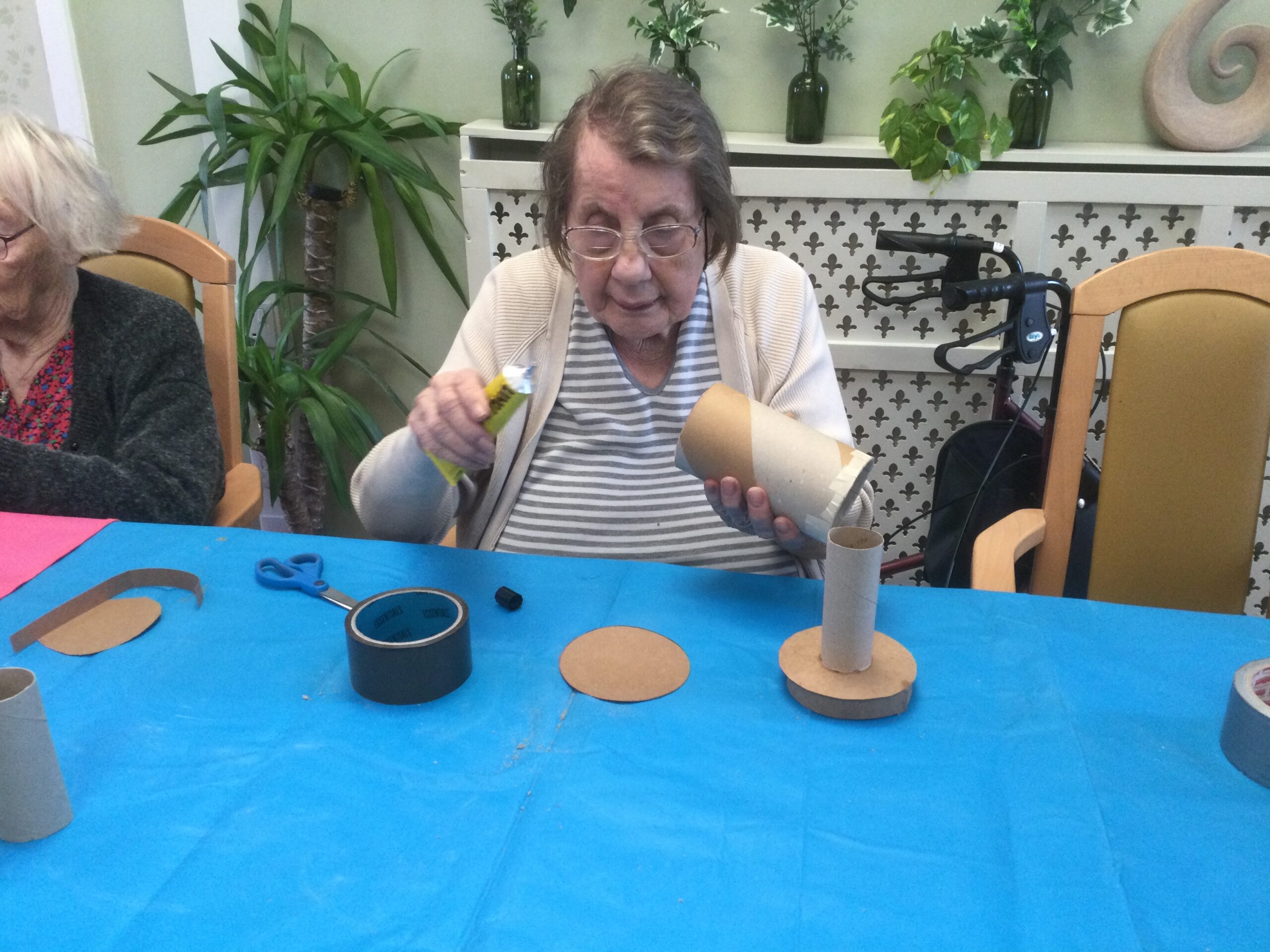 A woman holds a tube of glue in one hand, a cardboard tube in the other, and looks intently at what she's about to do