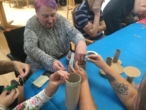 Several pairs of hands reach onto a table, sticking tape onto cardboard tubes