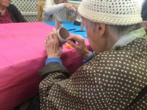 A woman wearing a raincoat and woollen hat holds a tube in one hand whilst applying tape with the other