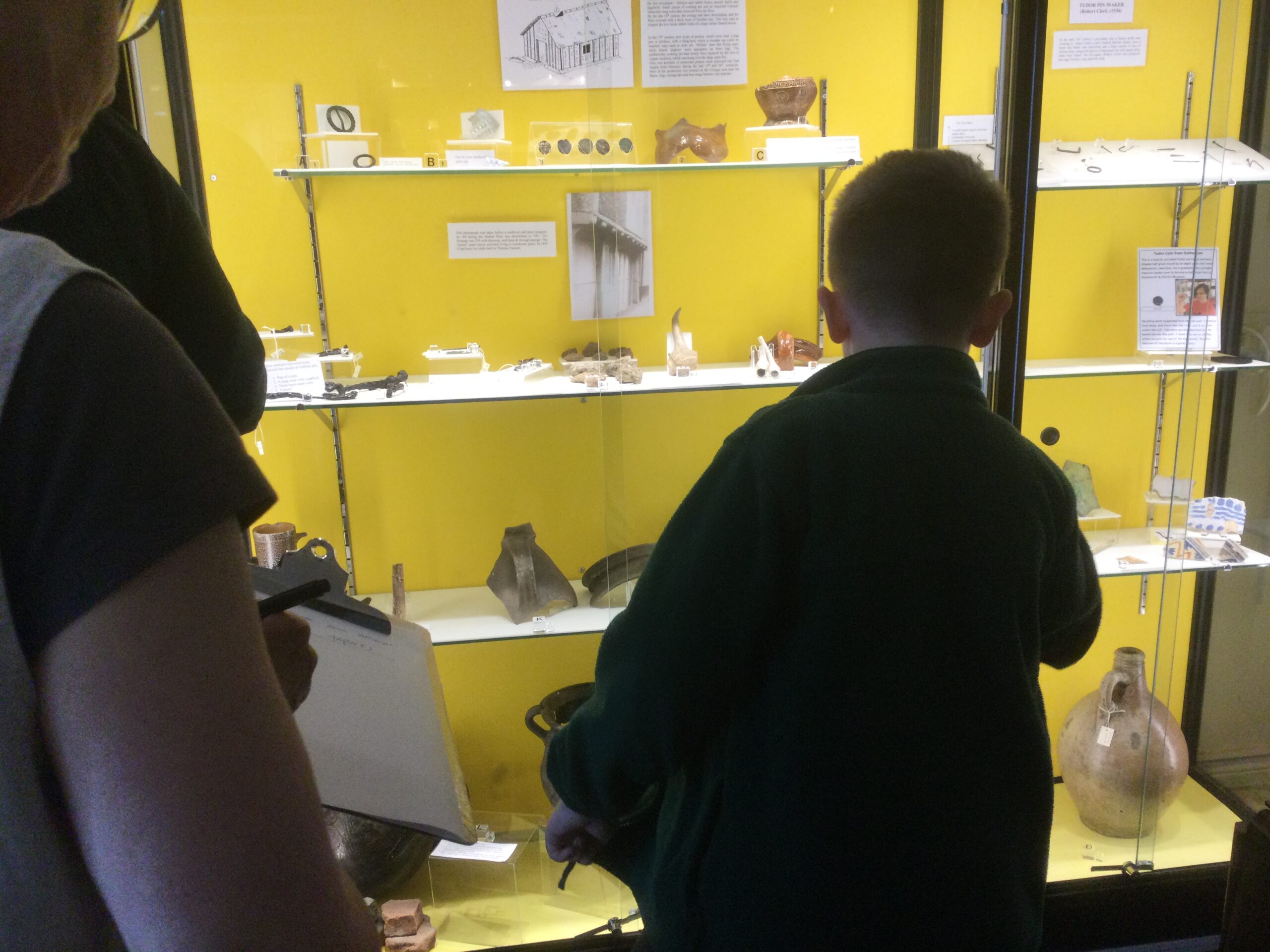 Children look into a display cabinet, with yellow background, containing pottery and coins dating from 15th century