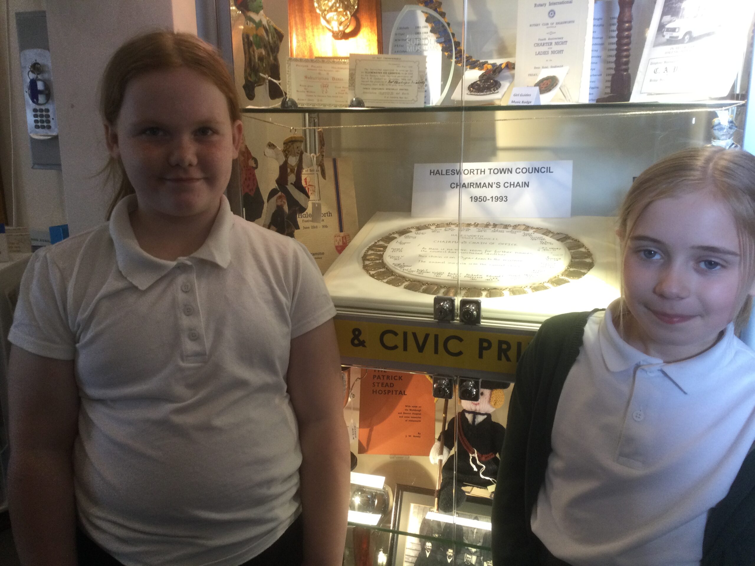 Two school girls stand in front of a display case showing the Halesworth Town Council Chairman's chain 1950 to 1993