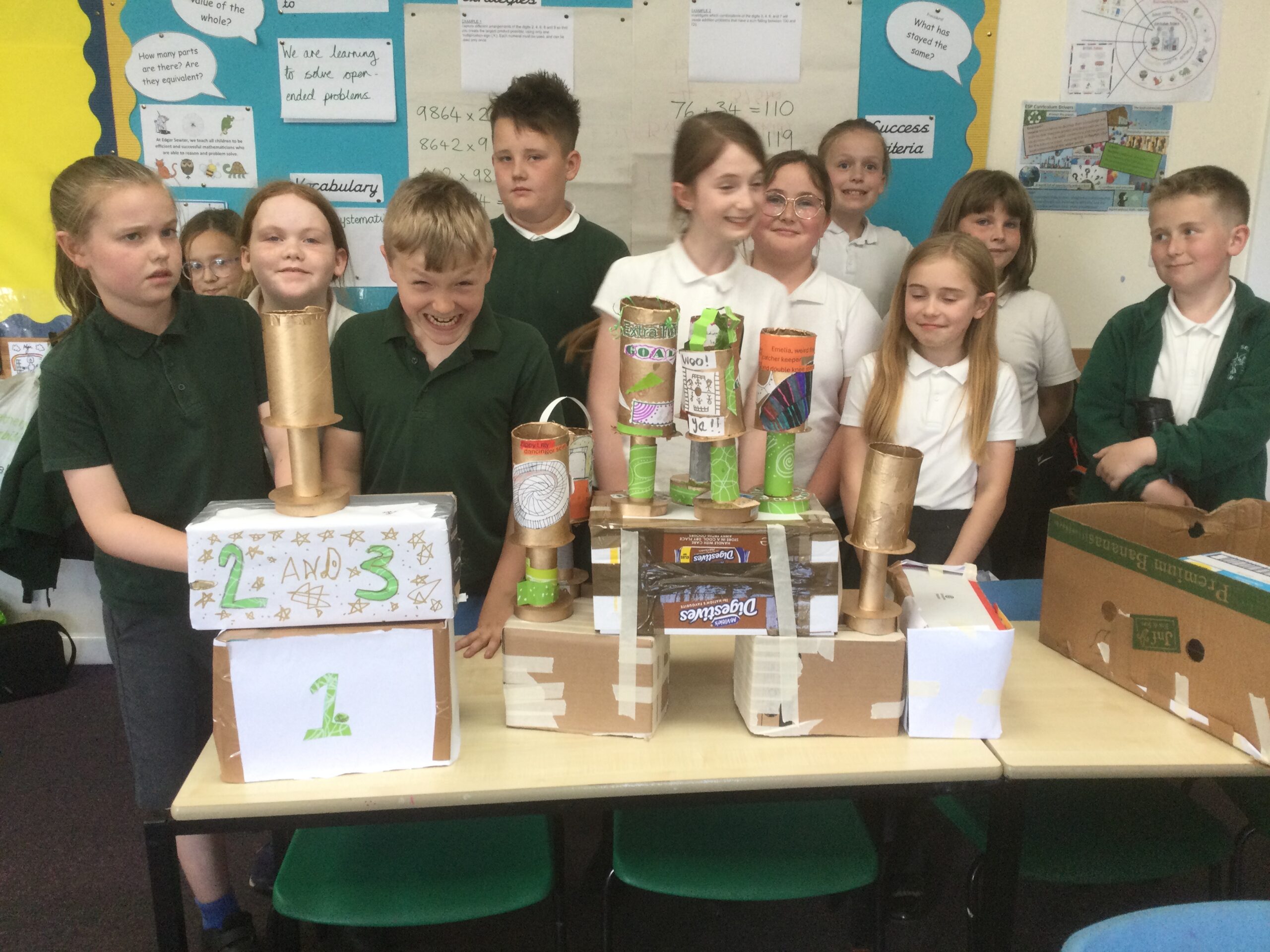 A group of school children stand behind an array of cardboard trophies on stands