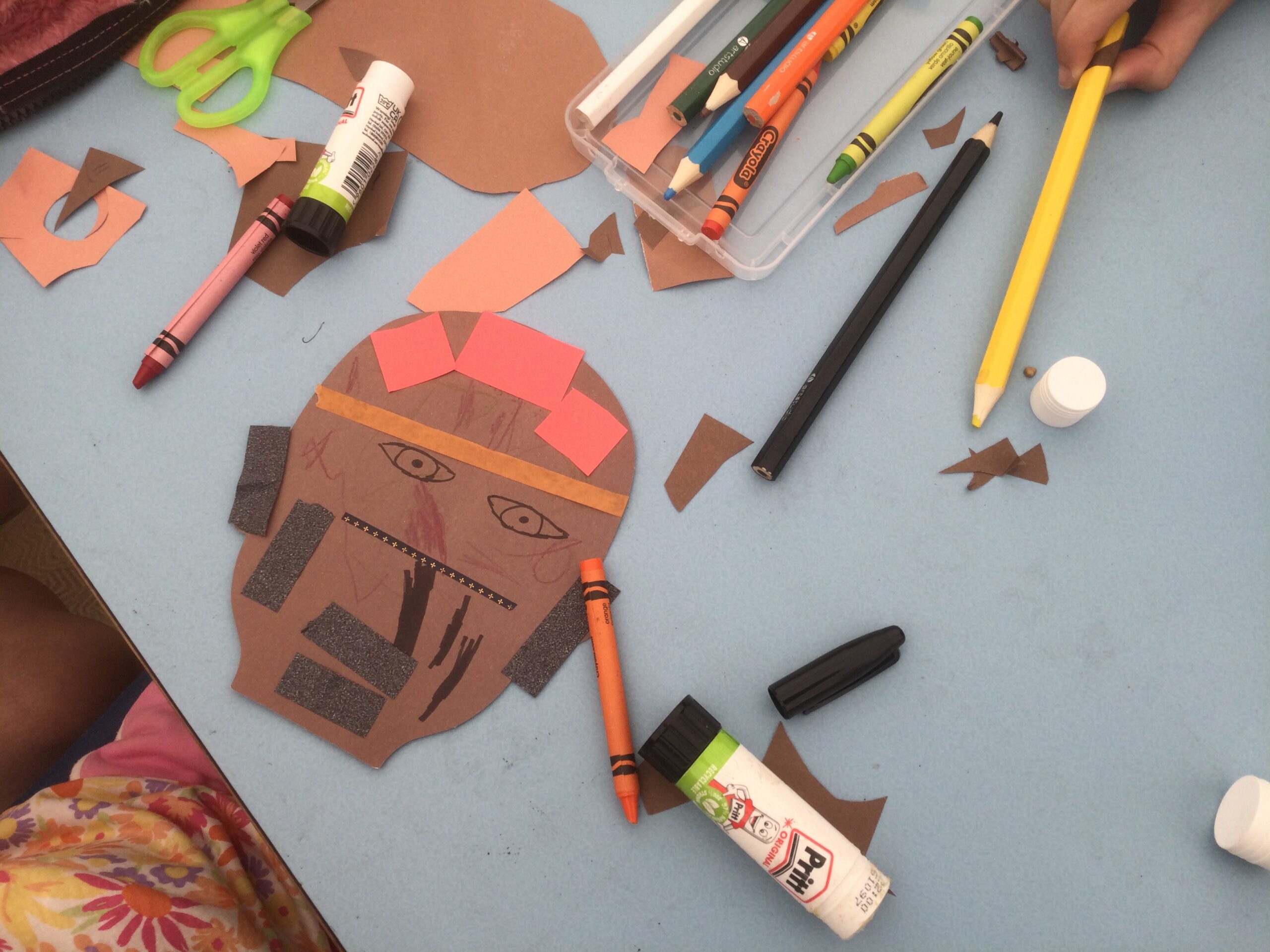 Overhead view of a paper cut out head and assorted crayons and glue