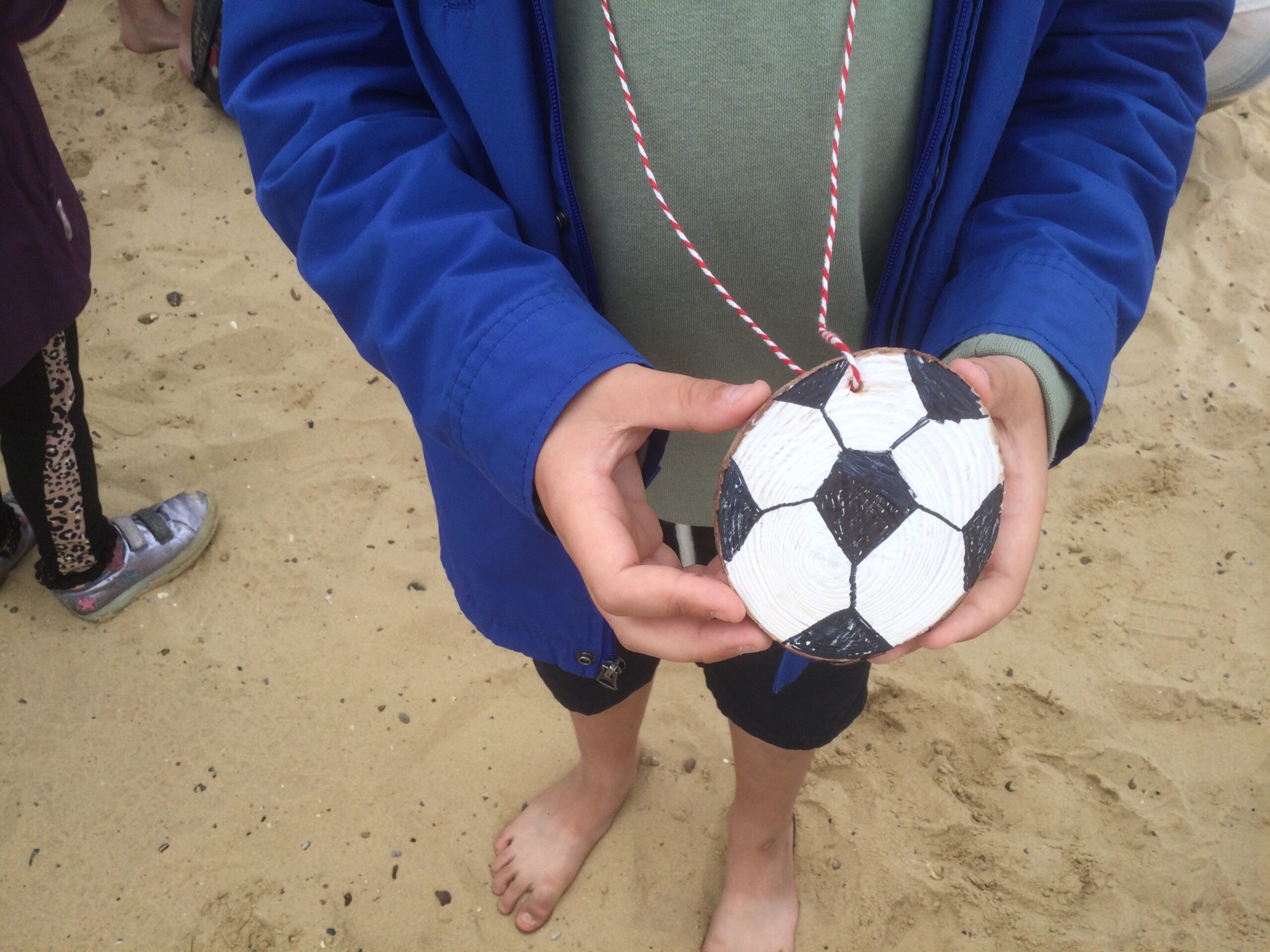 A child's hands holding a wooden medallion coloured in black and white to resemble a football