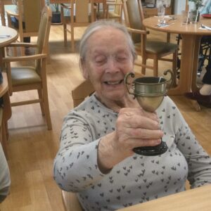 A woman smiles broadly whilst holding up a trophy