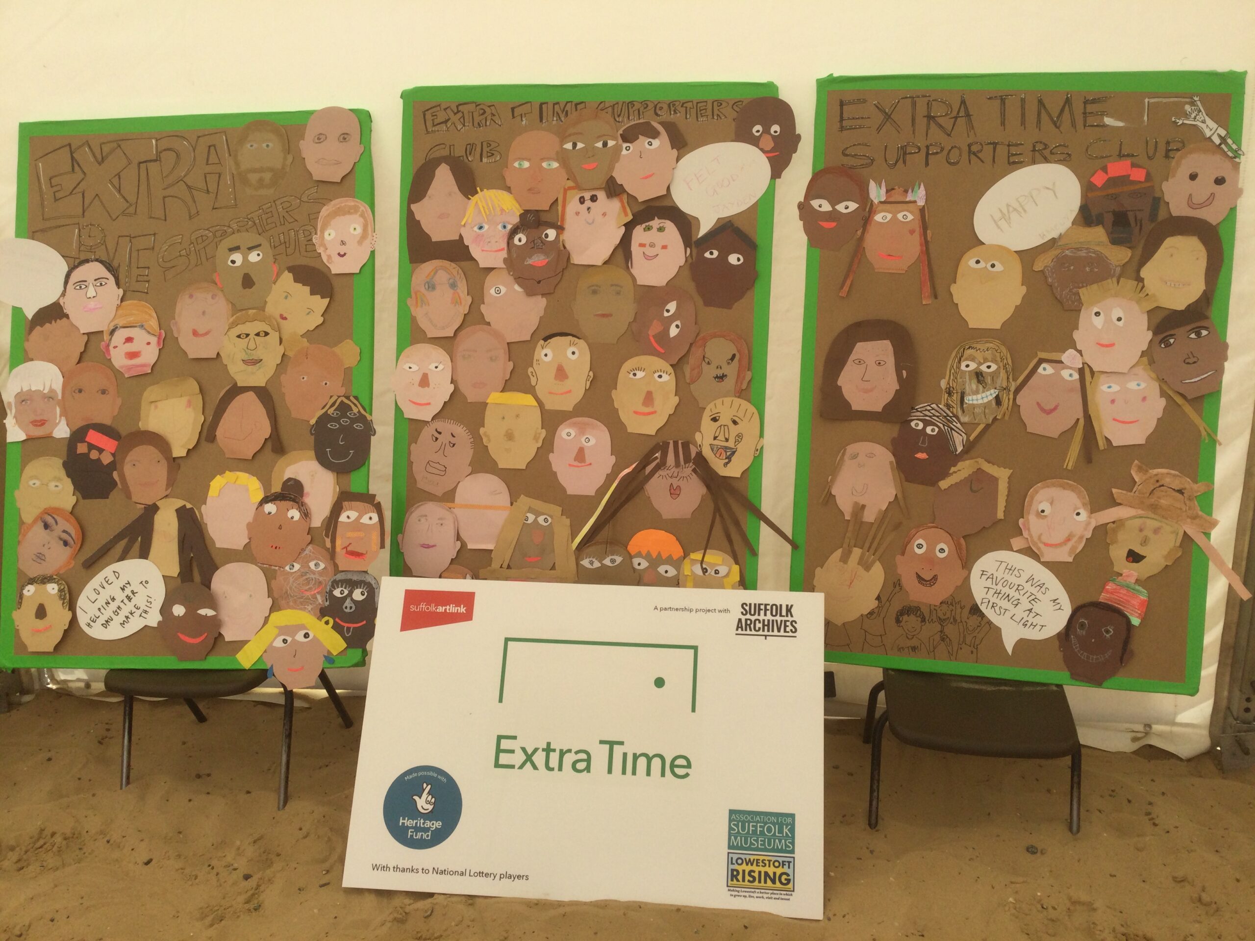 Three cardboard panels with lots of cut out self portraits and words Extra Time Supporters Club. Logo board in front credits funders and says Extra Time