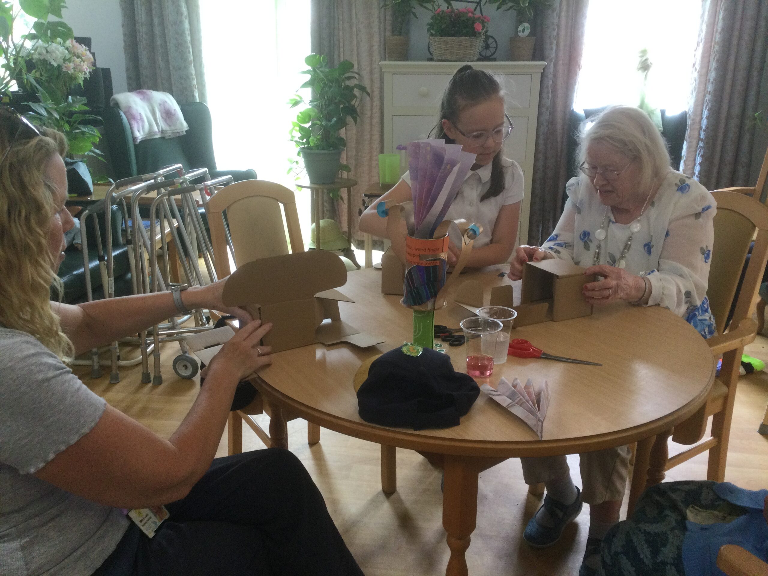 A round table seated at which are two adults and a child. They are all folding crdboard boxes into cub shapes