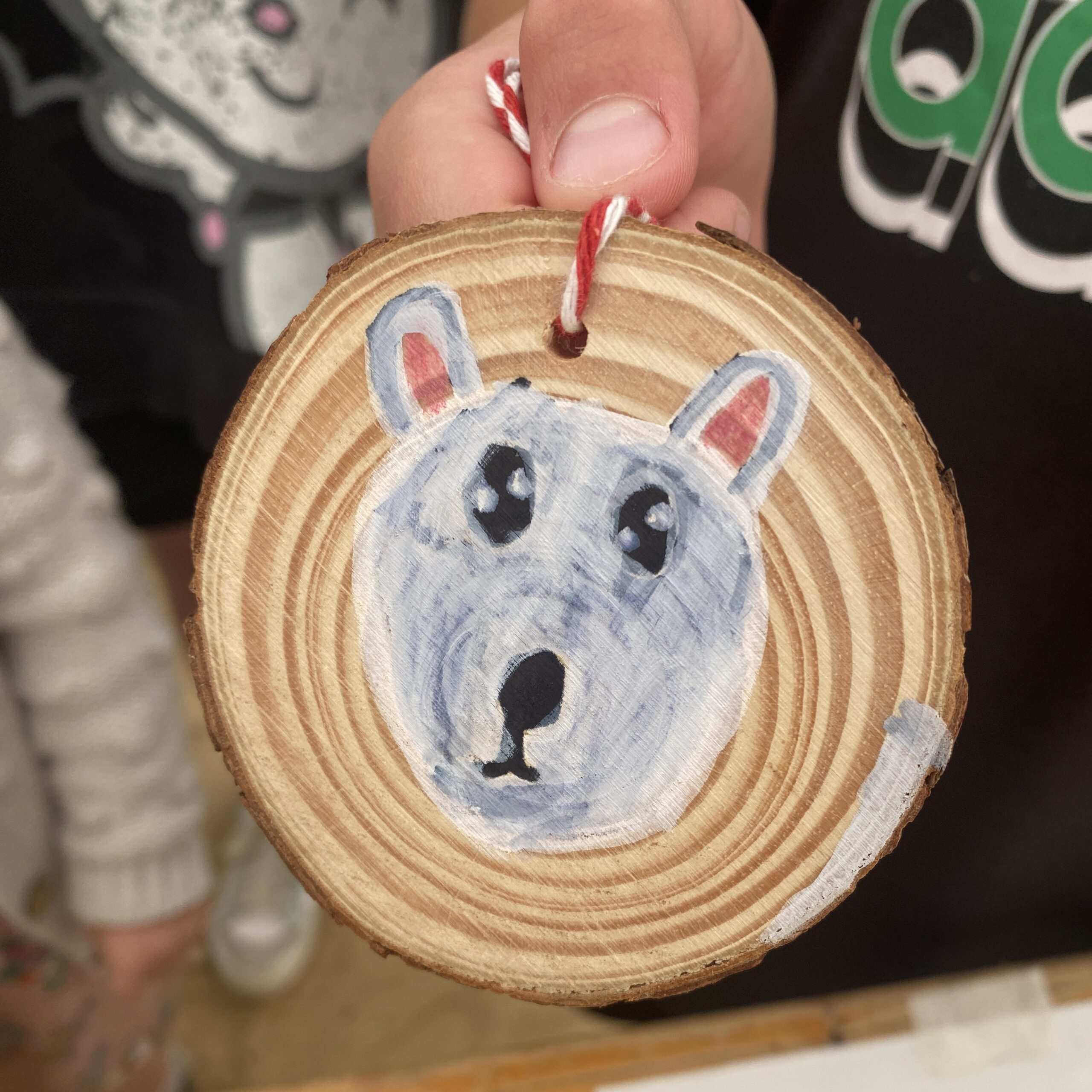 A child hand holding a wooden disc decorated with drawing of a dog