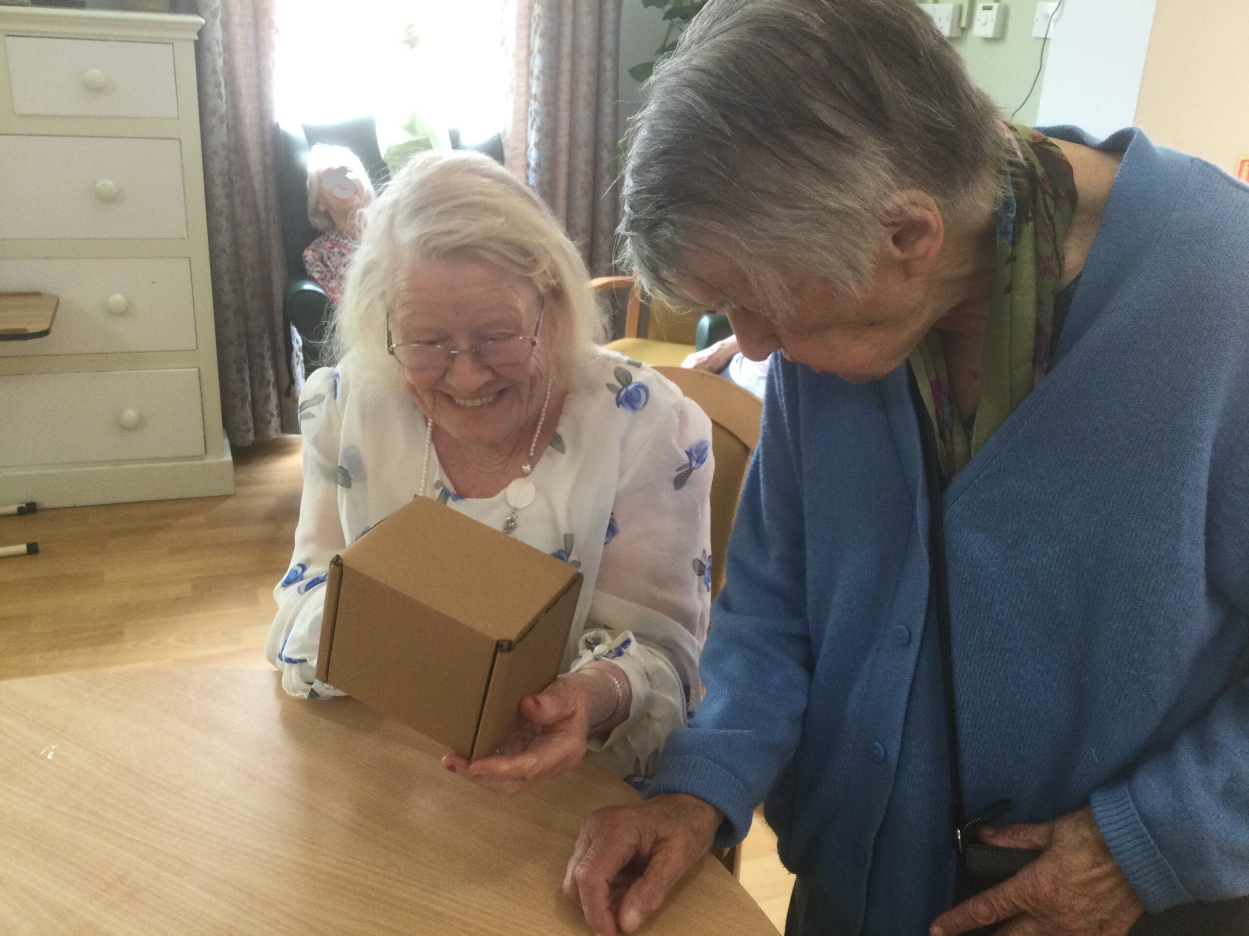 A woman holding a cardboard cube, clearly pleased with the results of folding it into place. Another woman looks on