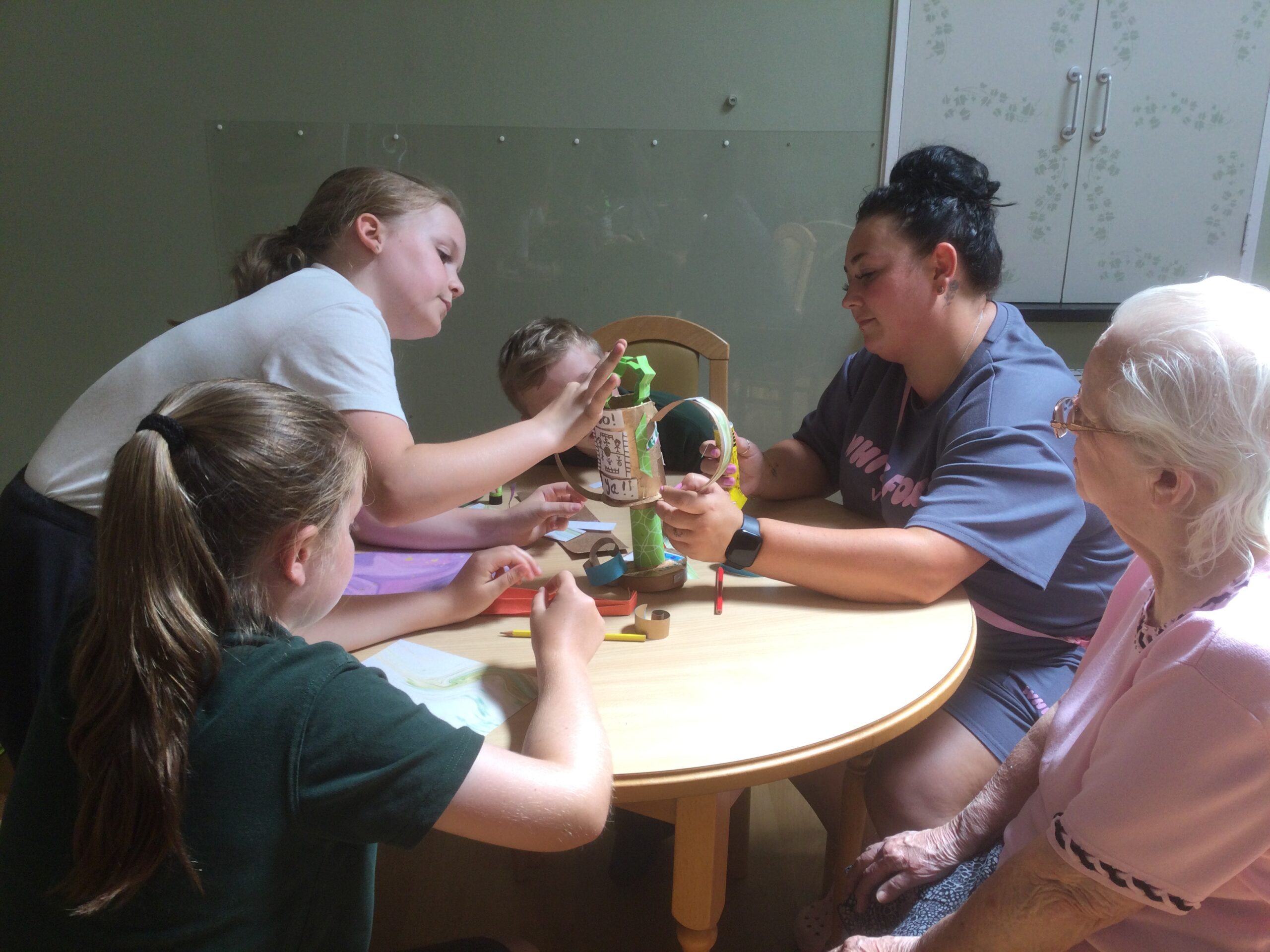 A small group of adults and children working together to glue a pair of card handles onto their handmade trophy