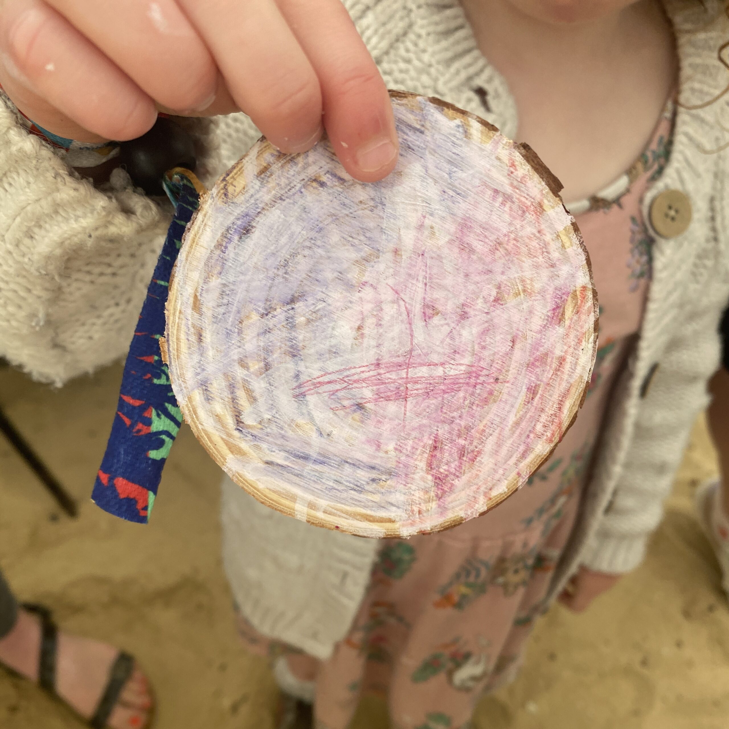 A child holds a wooden disc decorated in soft colours and overlaid with white