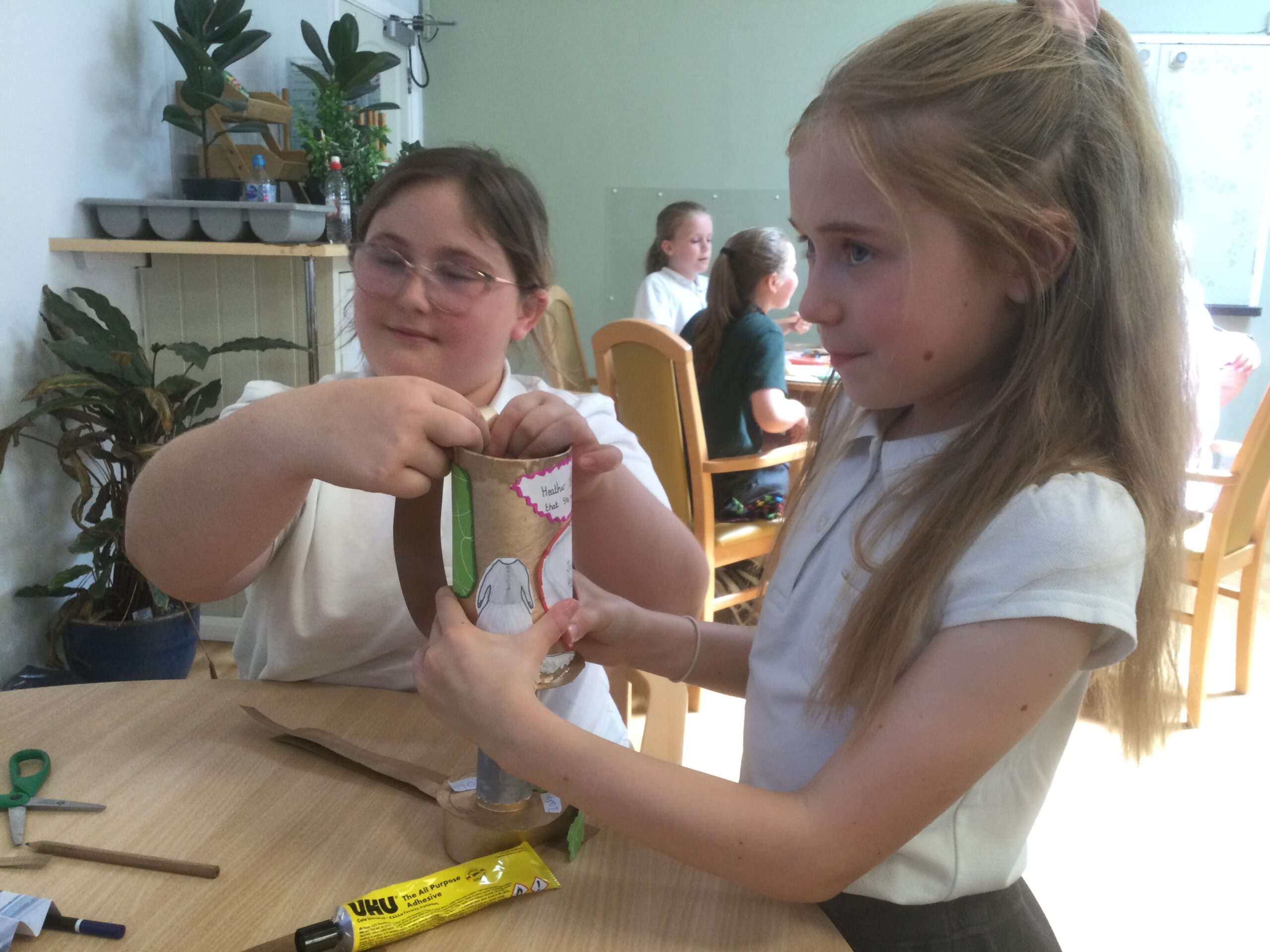 Two school girls holding a card handle in place whilst the glue dries