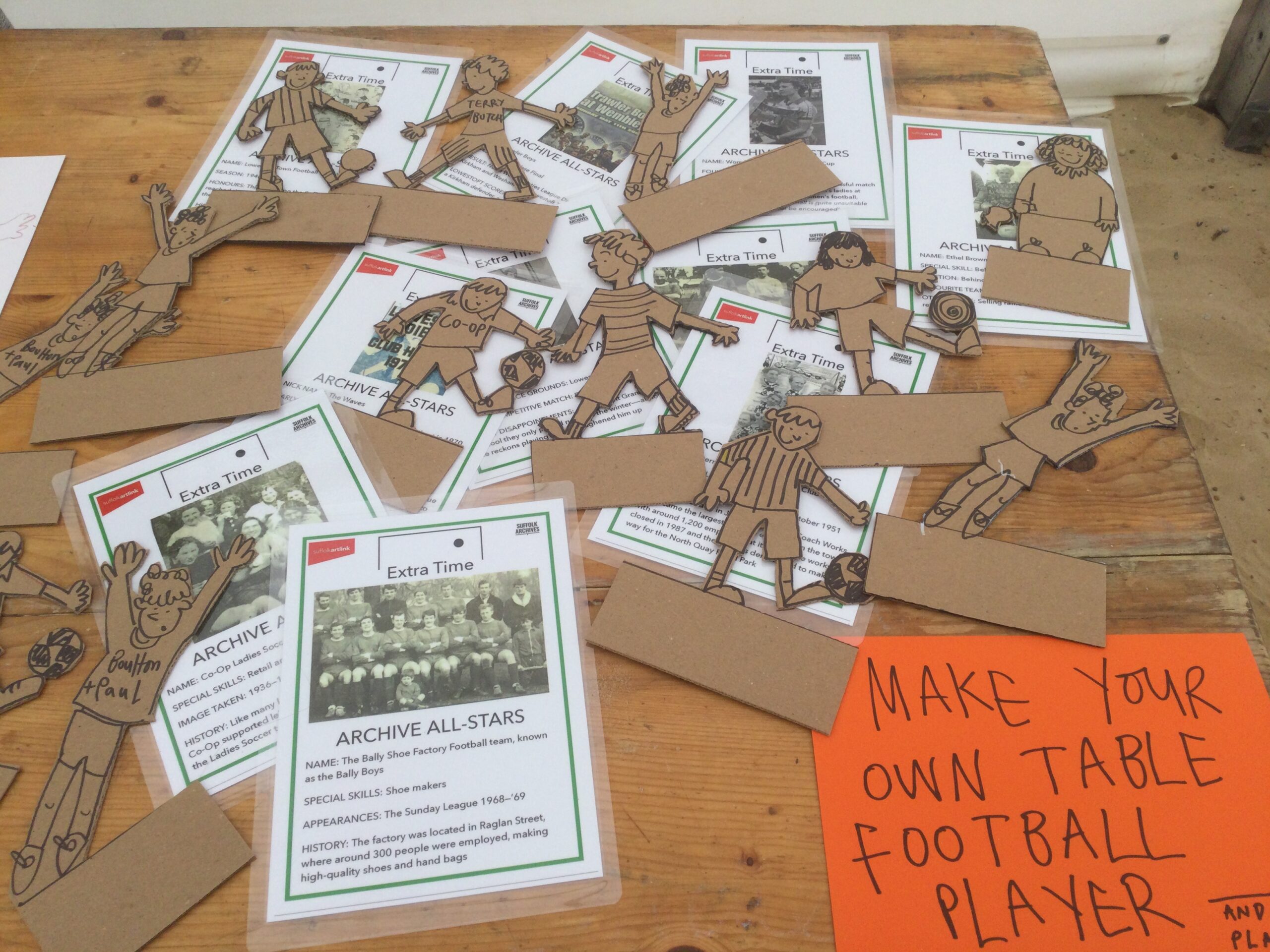 A variety of laminated cards referencing football characters are overlaid with cardboard cut out figures and invitation to Make Your Own Table Football Player