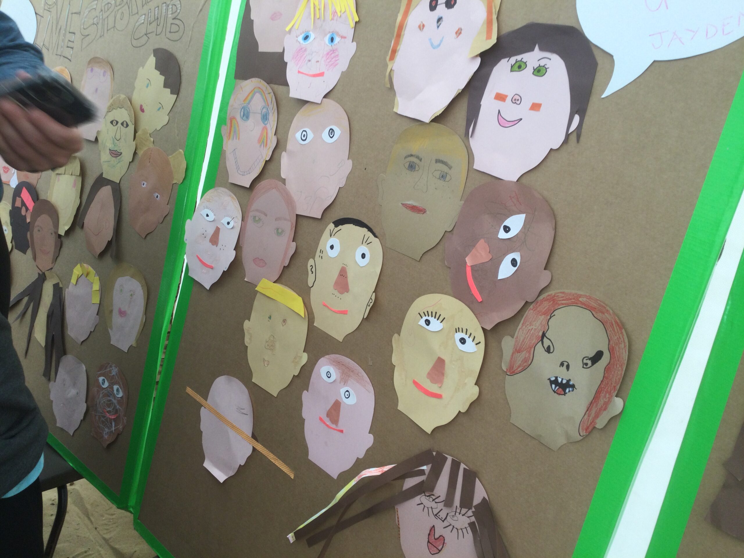 A variety of cut out self portrait faces on a cardboard panel