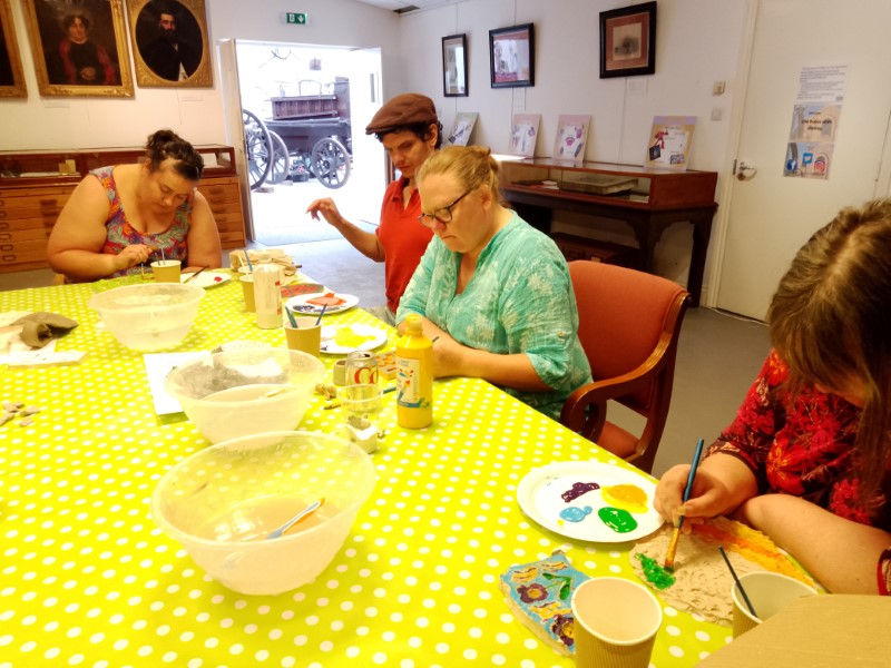 Creative participants sitting at a table painting plaster cast tiles