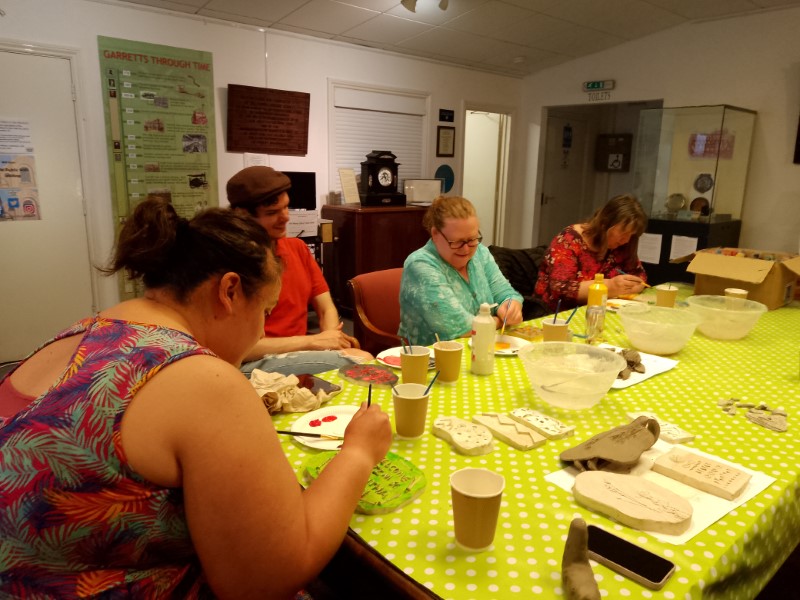 Creative participants sitting at a table painting plaster cast tiles