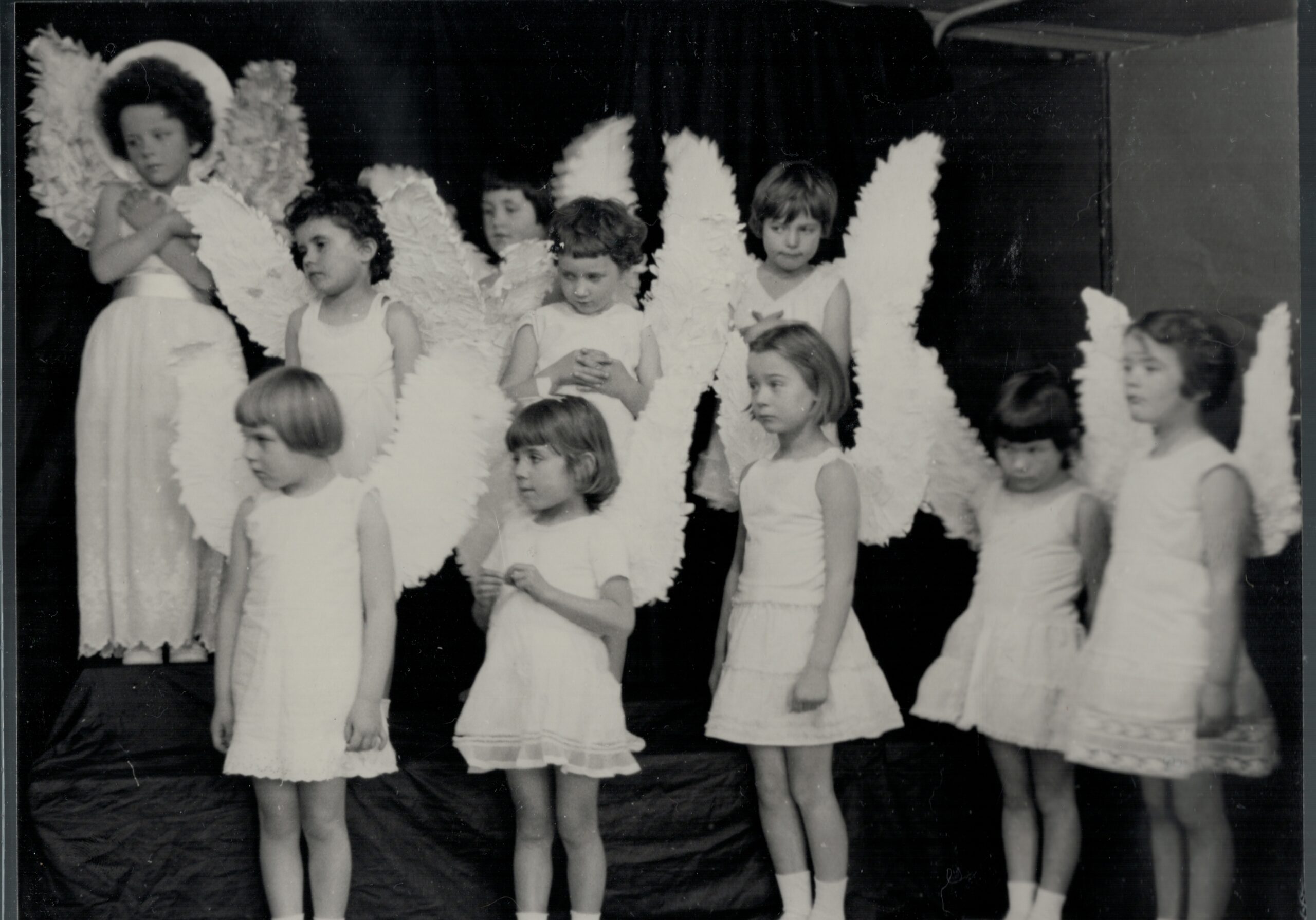 10 school girls dressed as angels with large wings attached to their backs, against a black backdrop