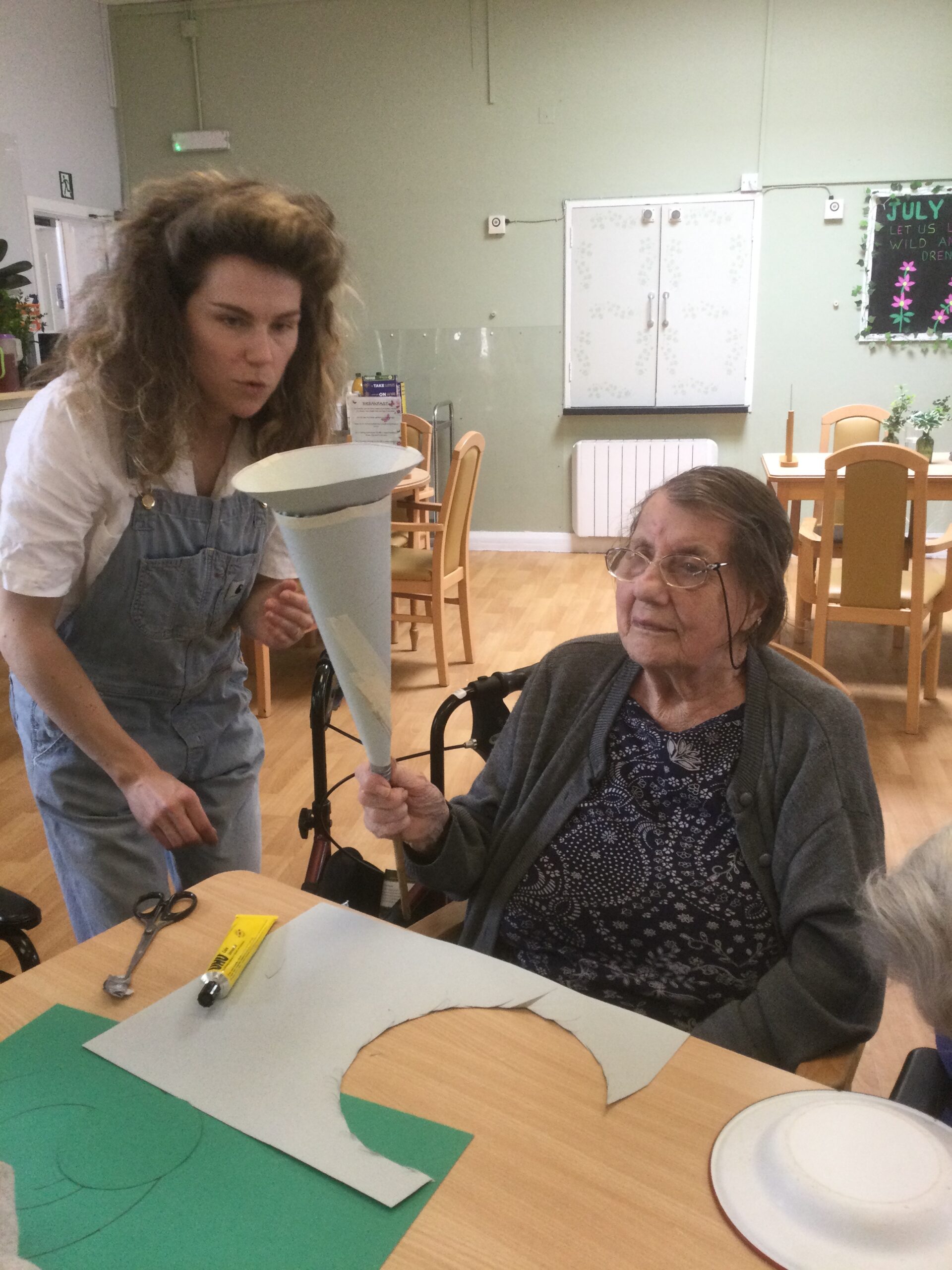 A woman holds a cardboard torch and together with another woman looks closely at it, checking that it's all glued properly