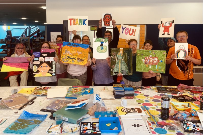 Learning disabled artists hold up artwork and colourful signs saying ‘thank you’.