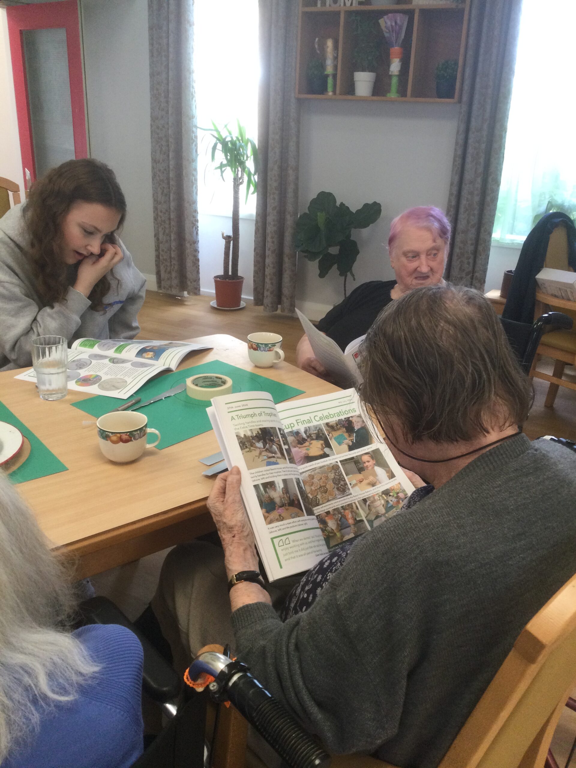 Three women seated at a table, all reading the Extra Time Souvenir Programme