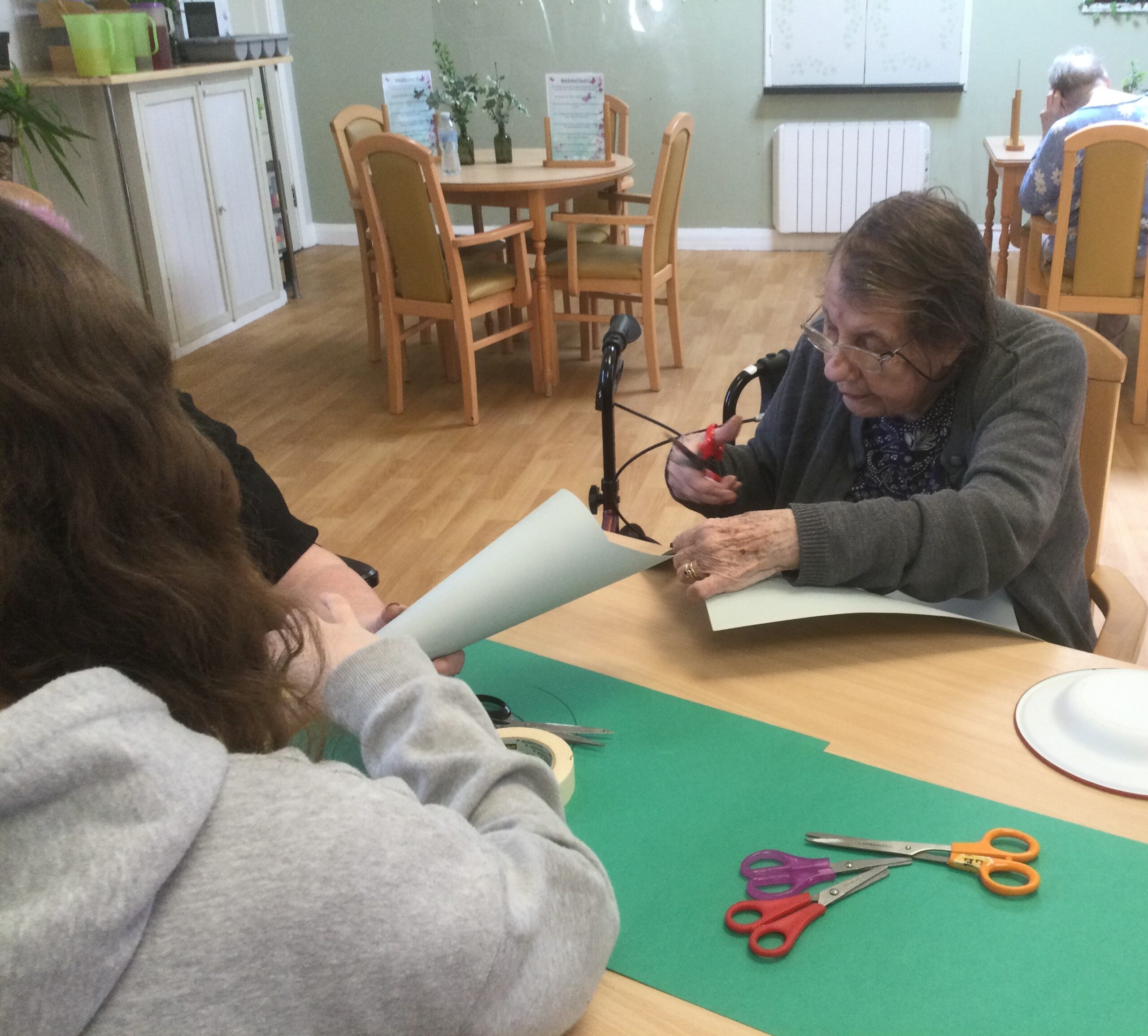 A woman with scissors in hand, trims the top of a paper cone, whilst another person looks on