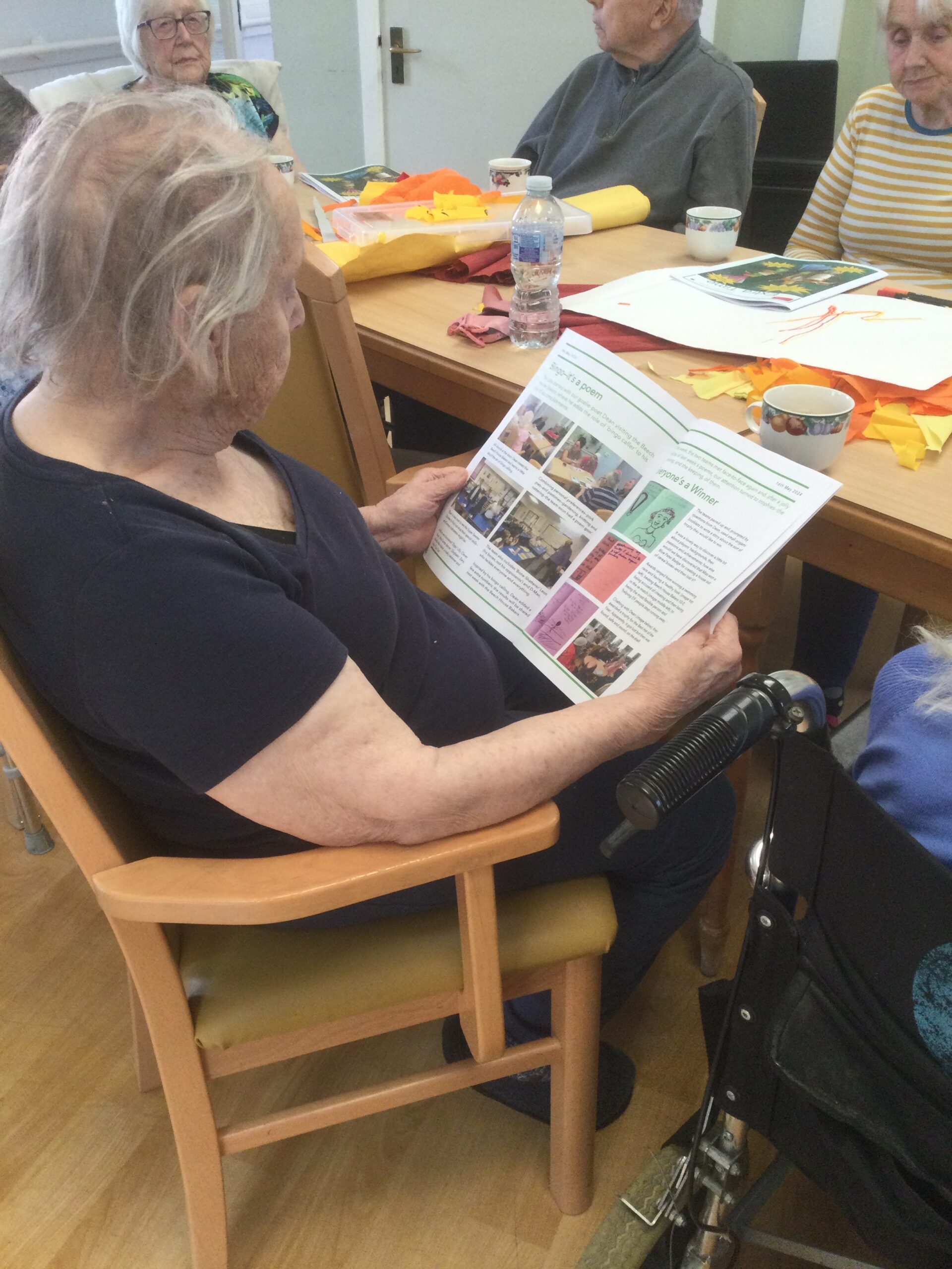 A woman seated at a table holds open a colourful magazine and is clearly looking at the pictures