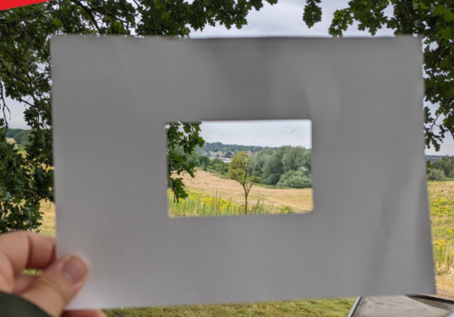 The landscape of Sutton Hoo framed by a handheld rectangular cardboard frame.