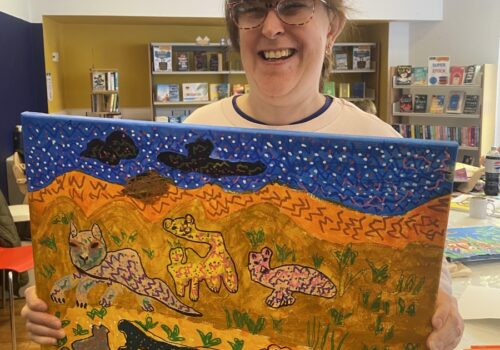 Caroline holding up painting of nightime desert scene with hills and animals.