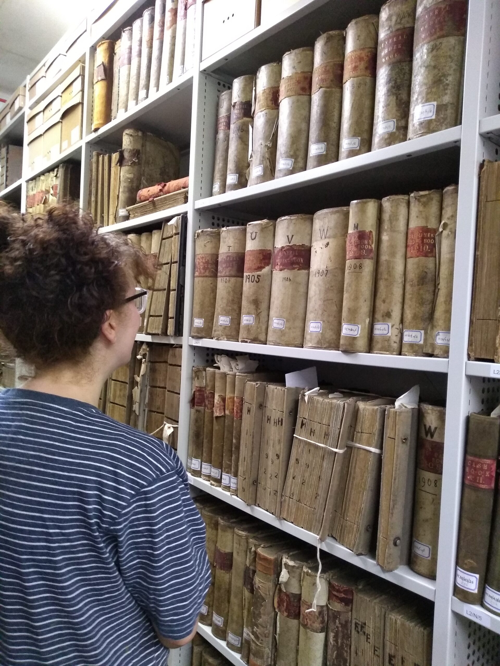 An adults stands in front of metal shelving full of old leather bound ledgers and sales books