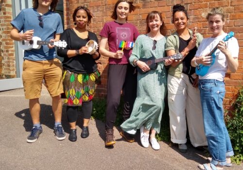 Group of 6 musicians holding ukuleles, tambourine, xylophone and bells.