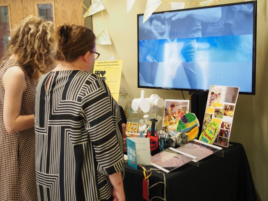 Two women looking at an exhibition stand of artwork