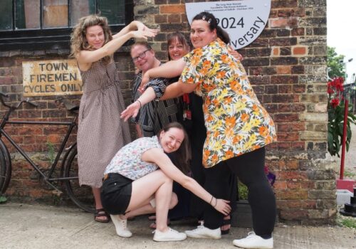 A group of women, laughing as the adopt a fun pose in front of The Long Shop, Leiston