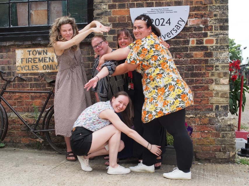 A group of women, laughing as the adopt a fun pose in front of The Long Shop, Leiston