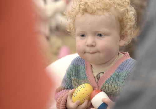 Child holding 2 patterned egg shakers