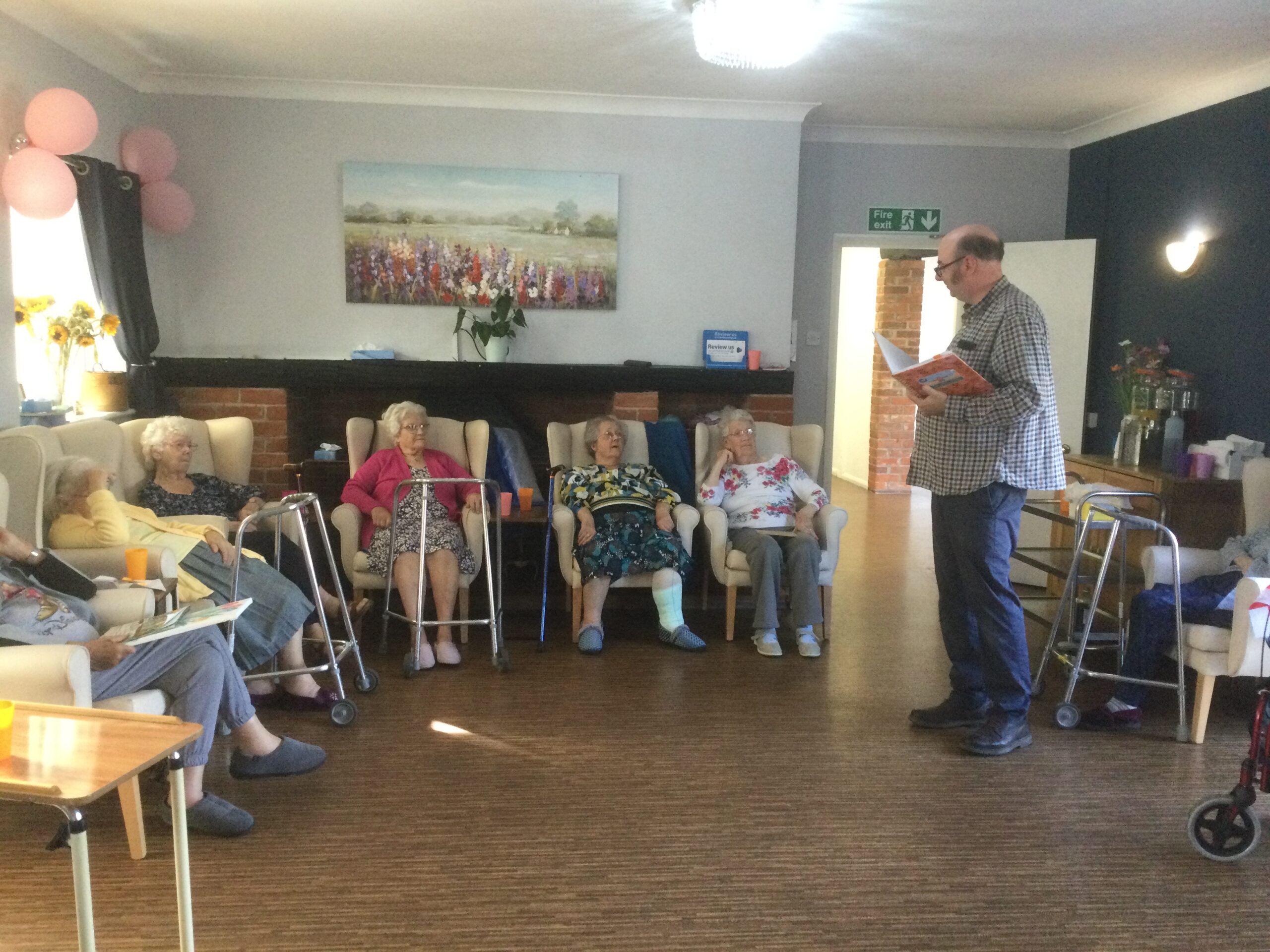 Dean Parkin stands in the middle of the room, surrounded by residents seated in armchairs, as he prepares to read out the poem