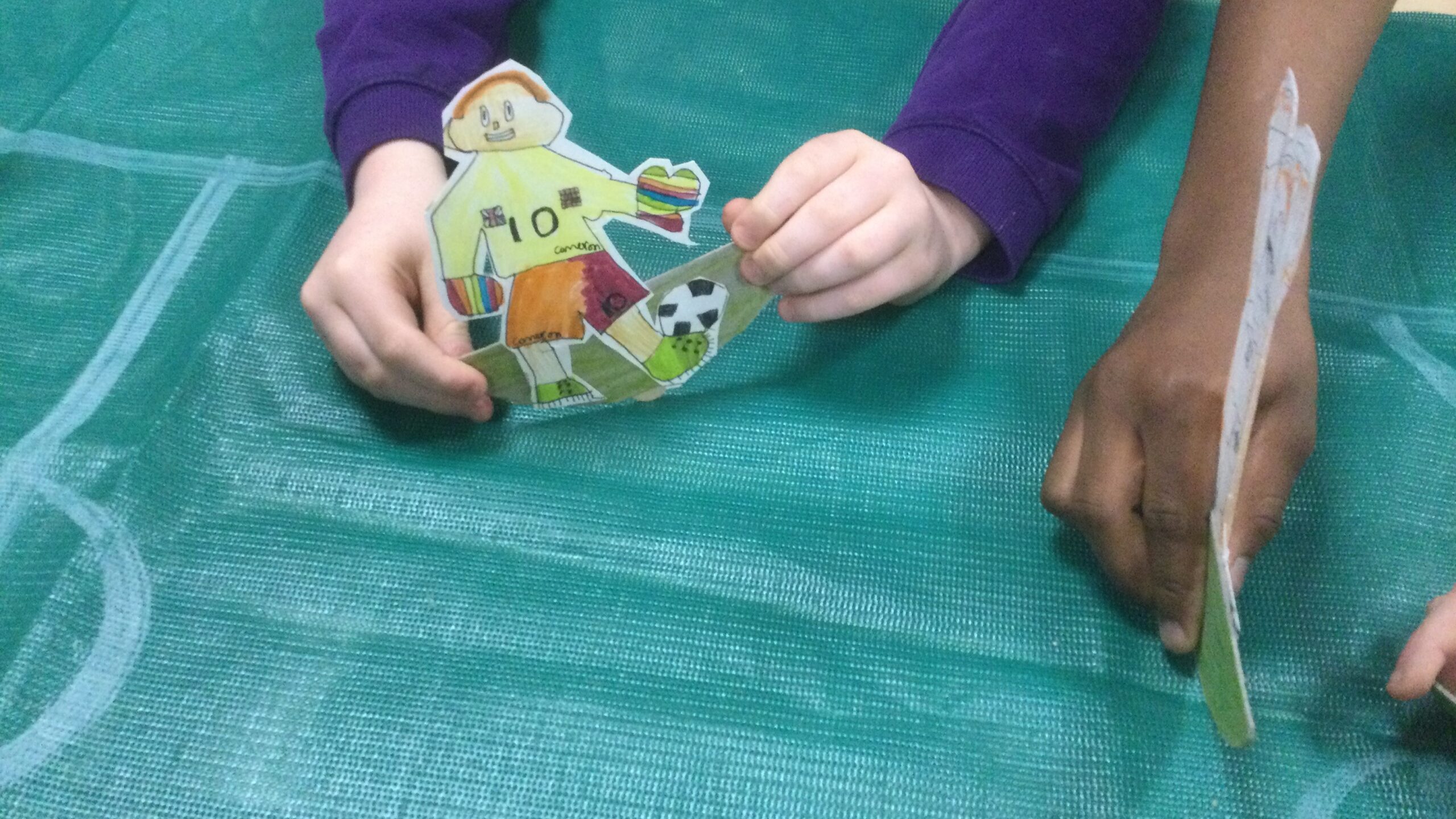 Children hands, holding cardboard football figures, one of which wears the number 10 jersey