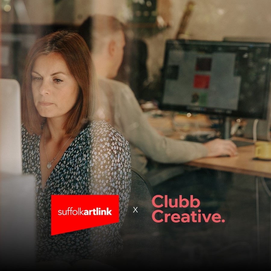 A woman and a man are working on computers with large monitors in an office. The woman is facing towards the camera and the man is facing away. The photo includes Suffolk Artlink and Clubb Creative's logos.