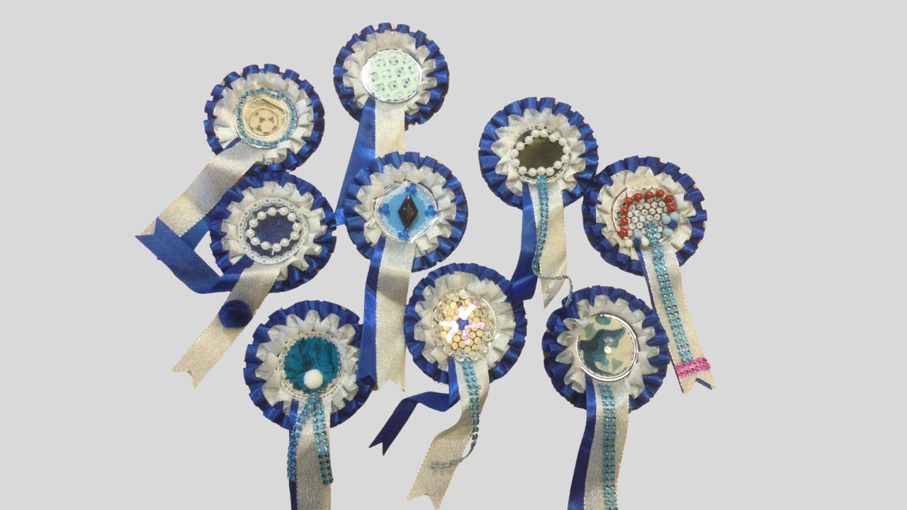 Nine hand decorated blue and white football rosettes, decorated with jewels, bobbles, sparkly braid and assorted papers