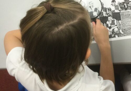 A child using a magnifying glass to study a monochrome photograph of a football team