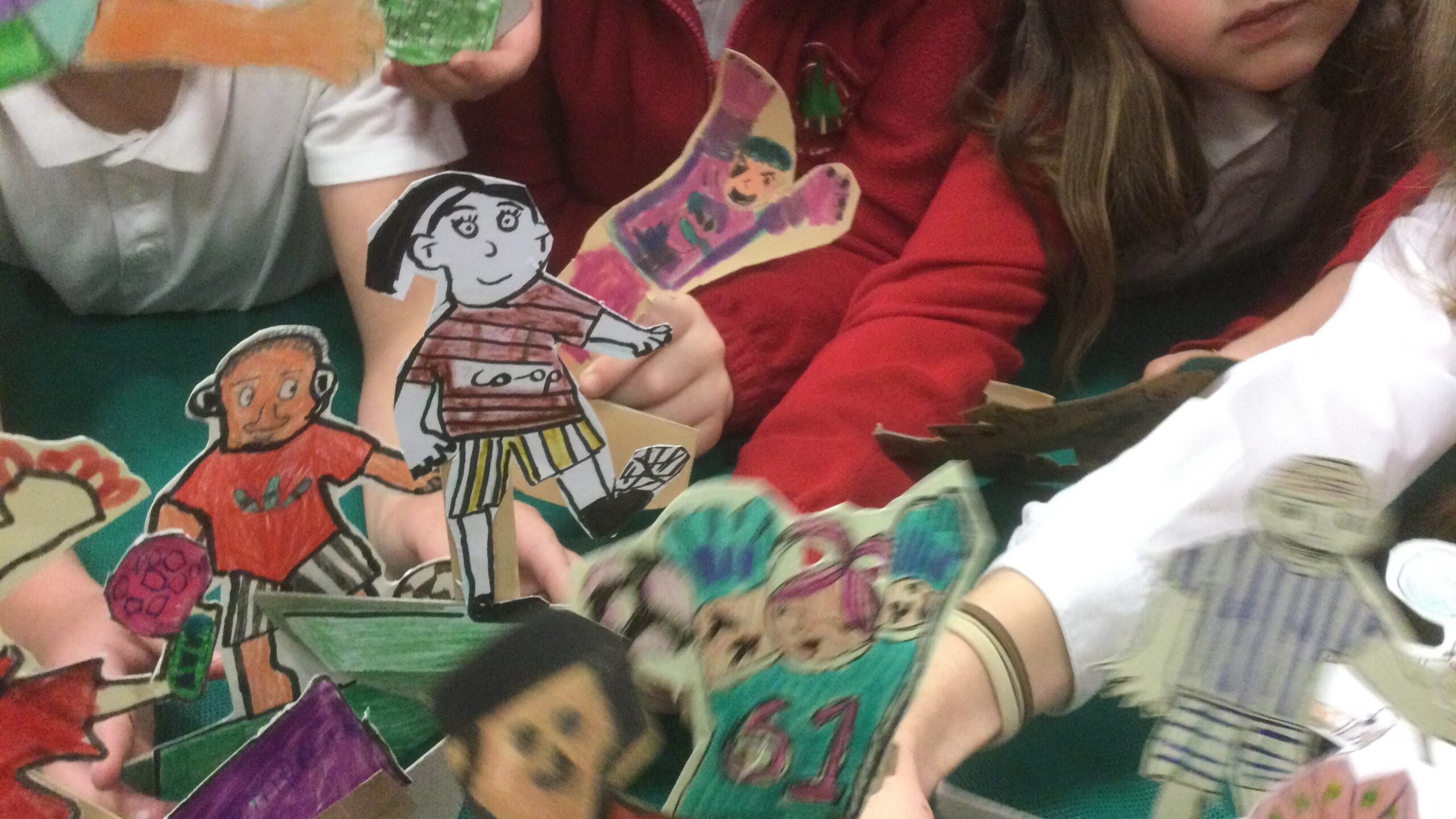 Children's outstretched arms holding a melee of cardboard football figures on the table in front of them