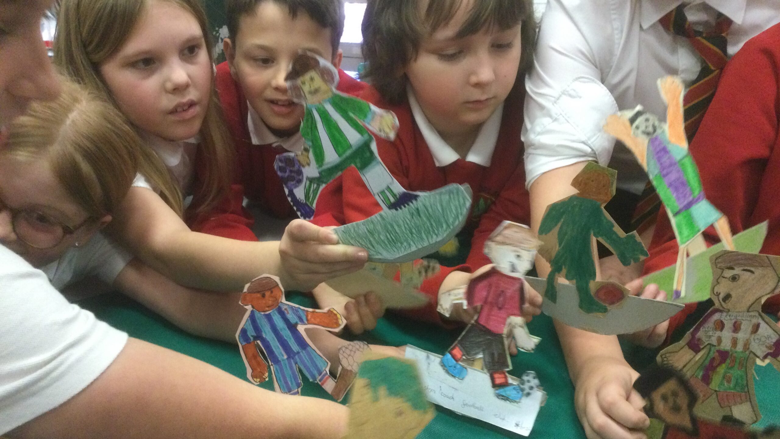 A number of school children, some dressed in red jerseys, holding cardboard football figures in front of them